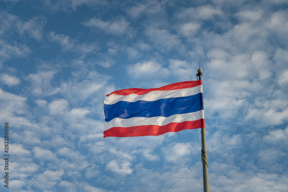 Thai national flag is waving by turbulent or severe wind direction, with background of blue cloudy sky.