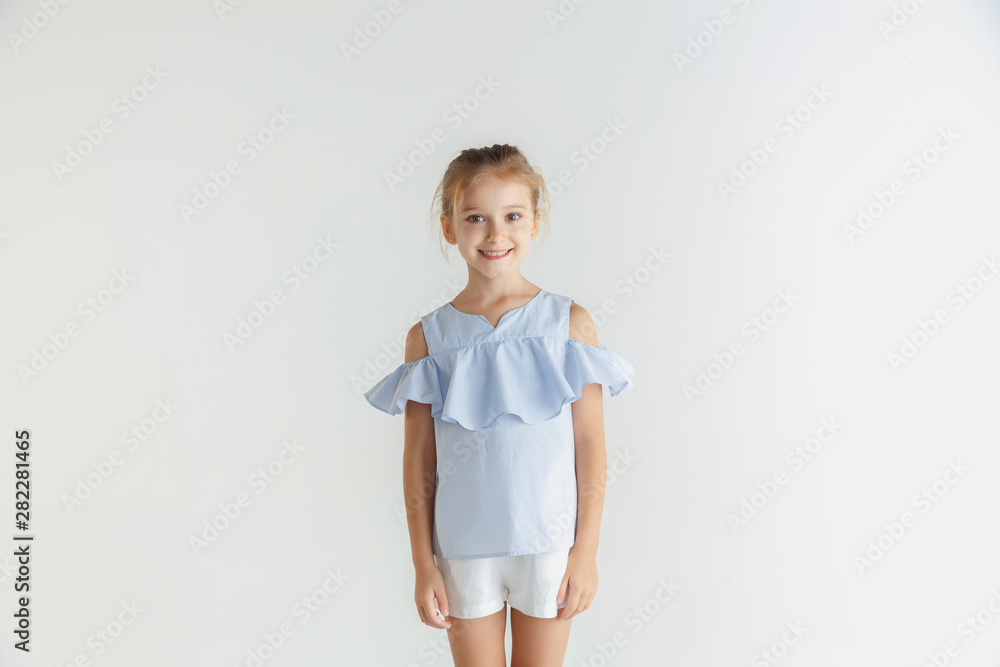 Stylish little smiling girl posing in casual clothes isolated on white studio background. Caucasian blonde female model. Human emotions, facial expression, childhood. Standing and smiling. Stylish little smiling girl posing in casual clothes isolated on white studio background. Caucasian blonde female model. Human emotions, facial expression, childhood. Standing and smiling.