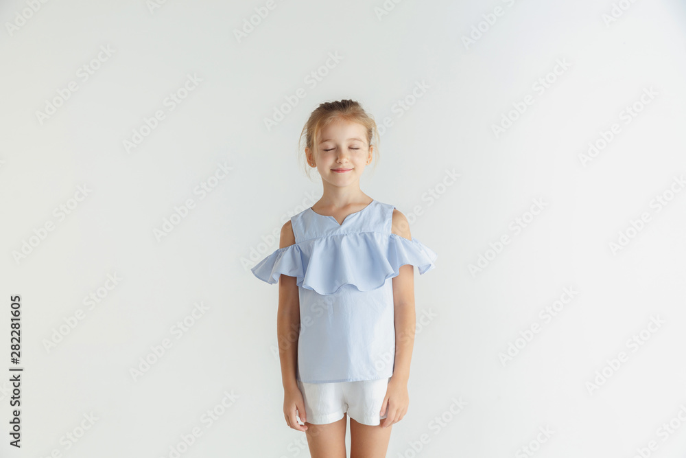 Stylish little smiling girl posing in casual clothes isolated on white studio background. Caucasian blonde female model. Human emotions, facial expression, childhood. Dreaming with eyes closed. Stylish little smiling girl posing in casual clothes isolated on white studio background. Caucasian blonde female model. Human emotions, facial expression, childhood. Dreaming with eyes closed.