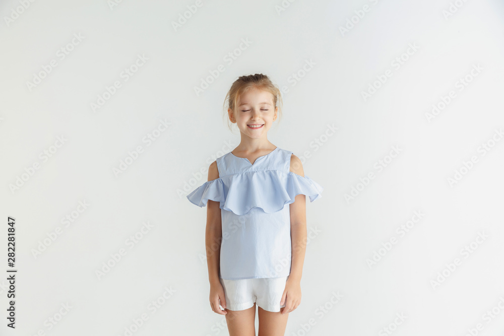 Stylish little smiling girl posing in casual clothes isolated on white studio background. Caucasian blonde female model. Human emotions, facial expression, childhood. Dreaming with eyes closed. Stylish little smiling girl posing in casual clothes isolated on white studio background. Caucasian blonde female model. Human emotions, facial expression, childhood. Dreaming with eyes closed.