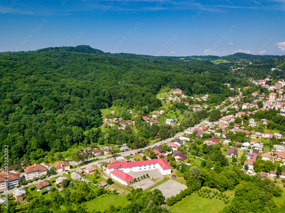 Drone view over the green forest and small city in mountainous area sunny day in summer season. Carpatians mountains, Romania.