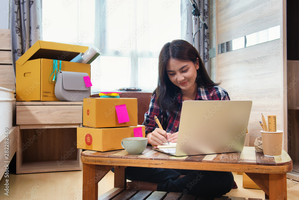 Asian business woman writes note on daily about order from customer product, Working at home office with eCommerce system. Small and Medium Enterprises Concept. Asian business woman writes note on daily about order from customer product, Working at home office with eCommerce system. Small and Medium Enterprises Concept.