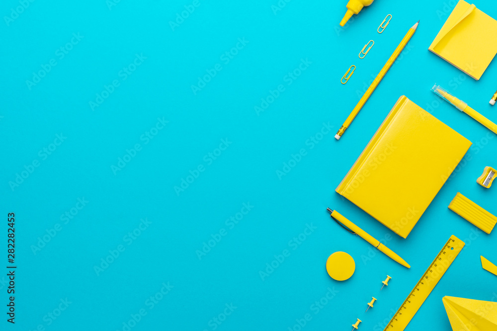 Fototapeta Top view photo of yellow stationery over turquoise blue background with copy space. Flat lay image of stickers, pencils, notebook, ball-point pen, eraser, sharpener, paerclips, pushpins and ruler.