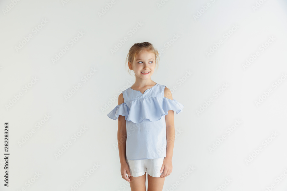 Stylish little smiling girl posing in casual clothes isolated on white studio background. Caucasian blonde female model. Human emotions, facial expression, childhood. Smiling, looking at side. Stylish little smiling girl posing in casual clothes isolated on white studio background. Caucasian blonde female model. Human emotions, facial expression, childhood. Smiling, looking at side.