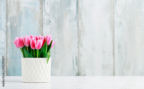 Fototapeta Naklejka Na Ścianę i Meble -  Pink tulips in white ceramic vase, wooden wall background.