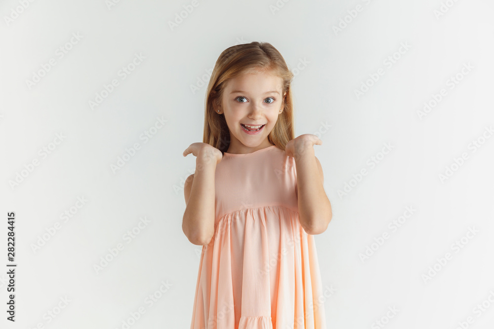 Stylish little smiling girl posing in dress isolated on white studio background. Caucasian blonde female model. Human emotions, facial expression, childhood. Smiling, astonished, wondered.