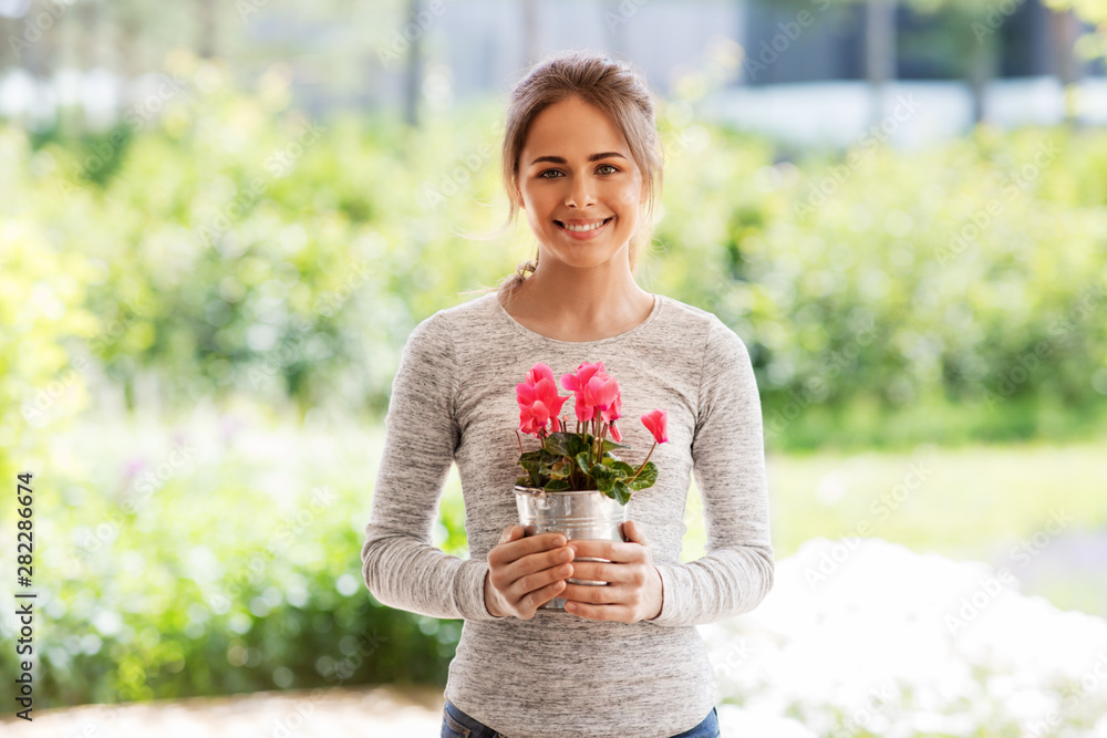 farming, gardening and people concept - happy young woman with pink cyclamen flowers in pot at summer garden farming, gardening and people concept - happy young woman with pink cyclamen flowers in pot at summer garden