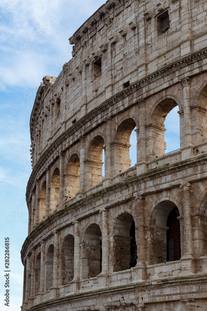 Detail of the Colosseum, under a blue sky with white clouds.