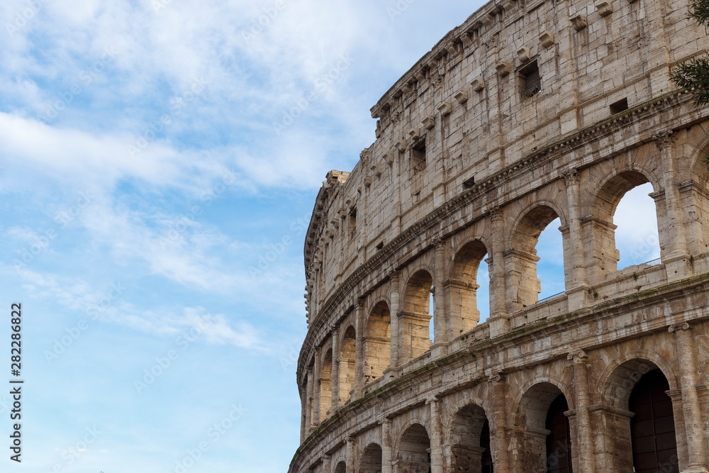 Detail of the Colosseum, under a blue sky with white clouds.
