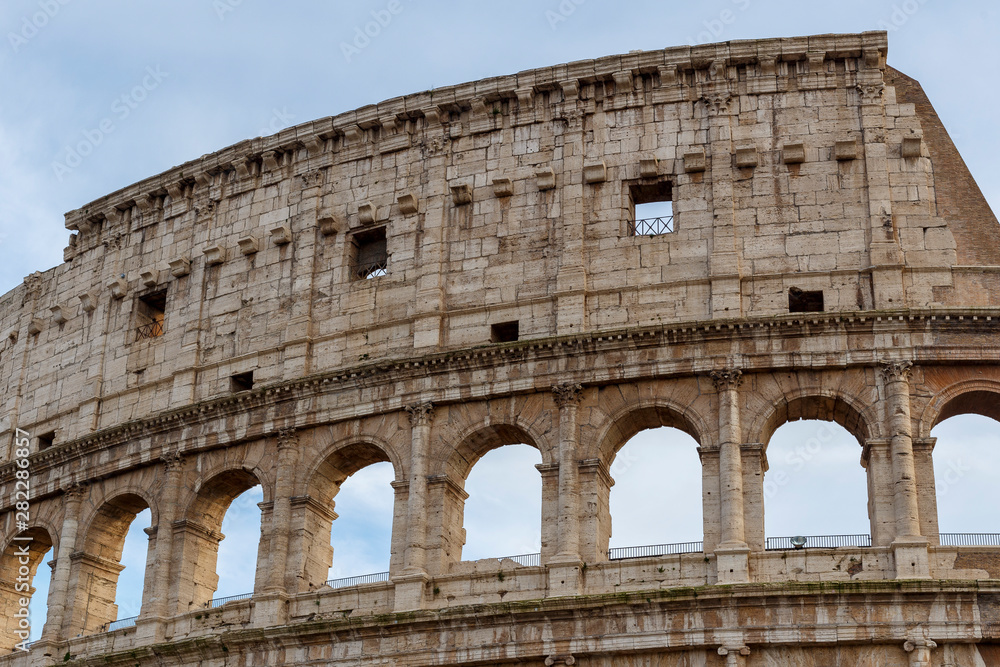 Obraz premium Detail of the Colosseum, under a blue sky with white clouds.