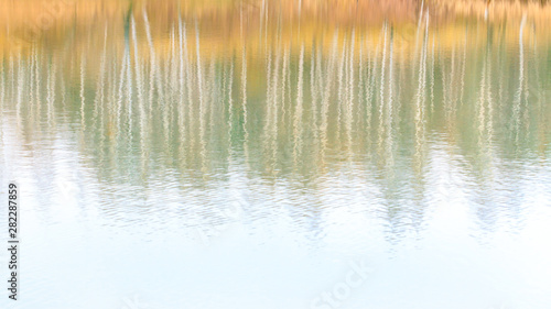Abstract blurred bright fall background in pastel shades. Reflection of autumn forest in the lake.