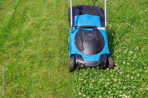 Electric lawn mower on a grass lawn with half mowed grass with copyspace