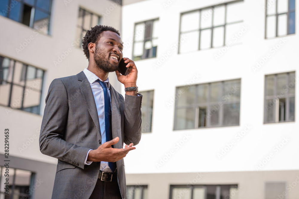 cheerful african american man gesturing and looking away while talking on smartphone cheerful african american man gesturing and looking away while talking on smartphone