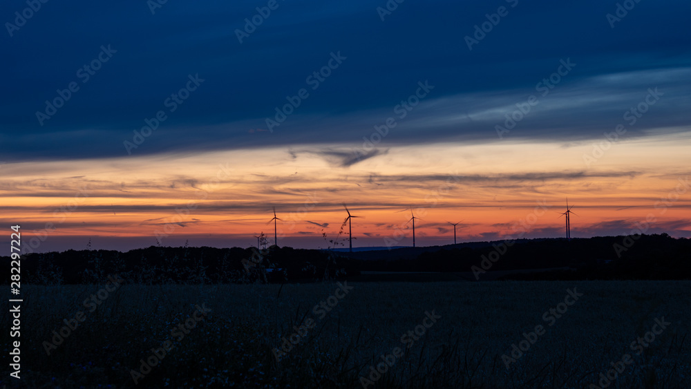 Cloudy sunset sky with silhouettes of wind turbines. 