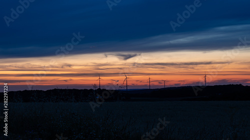 Cloudy sunset sky with silhouettes of wind turbines. 