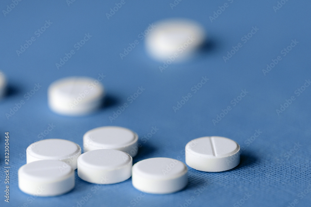 White tablets scattered on a blue background close up White tablets scattered on a blue background close up