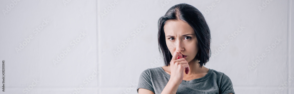 panoramic shot of sad pensive woman touching chin and looking at camera at home panoramic shot of sad pensive woman touching chin and looking at camera at home