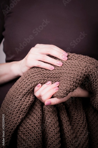 Beautiful female hands holding brown knitted sweater. Manicure with pink nail polish. Cozy concept