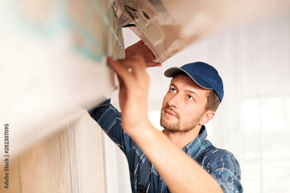 Young workman in workwear trying to find out reason of air conditioner disorder Young workman in workwear trying to find out reason of air conditioner disorder