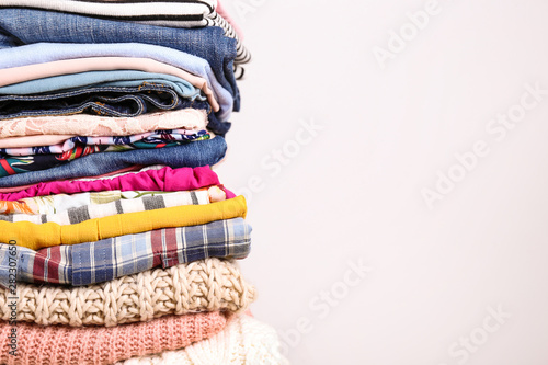Stack of clean freshly laundered, neatly folded women's clothes on wooden table. Pile of shirts, dresses and sweaters on white board, concrete wall background. Copy space, close up, top view.