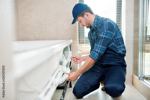 Bild auf Leinwand Contemporary technician in workwear installing pipe system by bathtub
