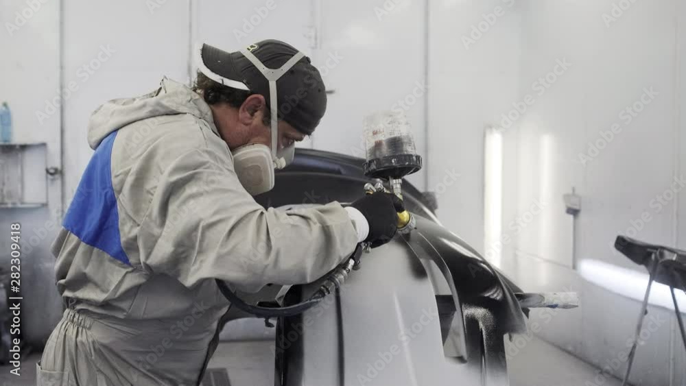 Man is painting parts of automobile in spray booth of car service. Man is painting parts of automobile in spray booth of car service.