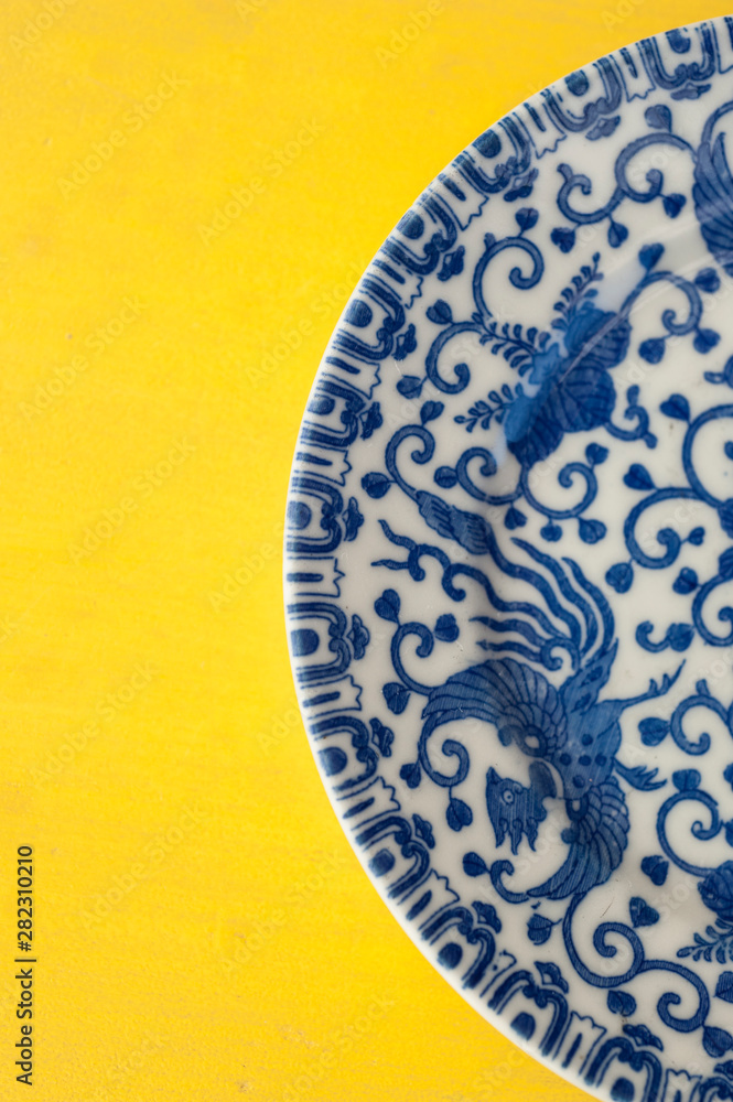 Blue Dragon Chinese China Plate set on a bright yellow table top. Still Life Photography.