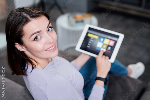 Happy young woman with digital tablet choosing something to watch at leisure