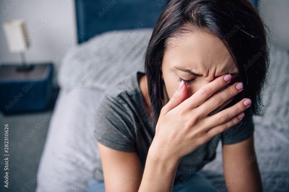 depressed woman sitting on bed at home, crying and covering face with hands depressed woman sitting on bed at home, crying and covering face with hands