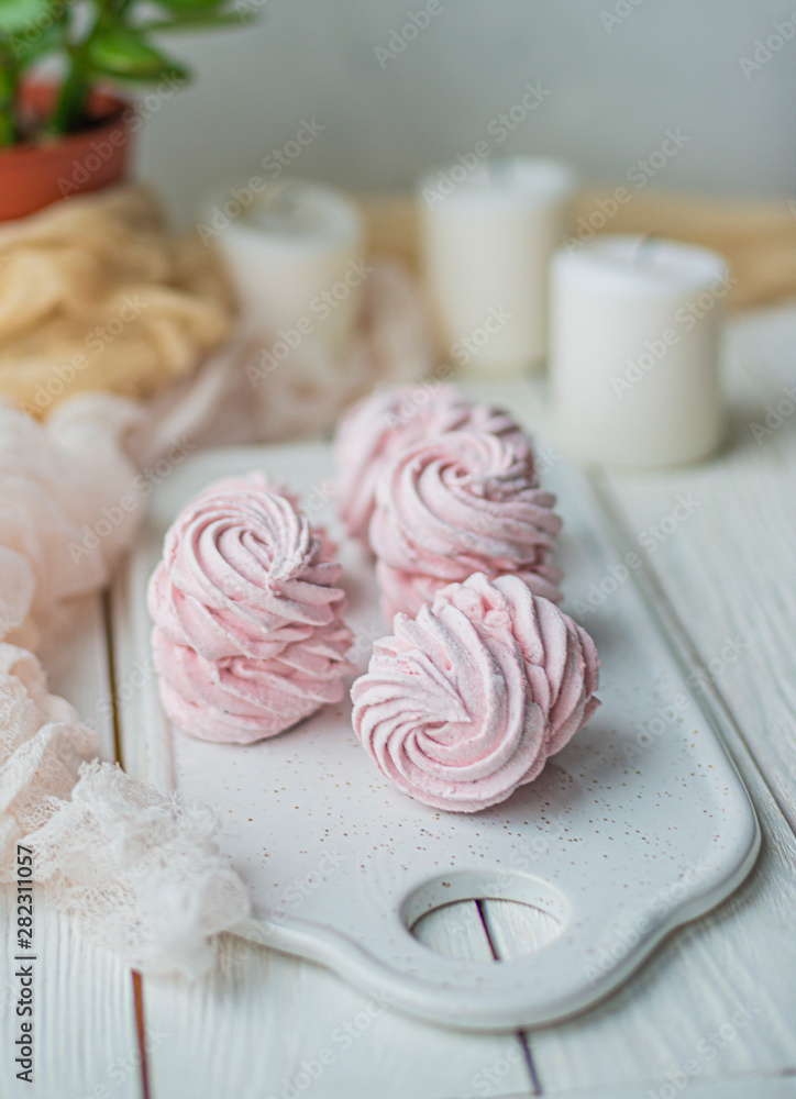 homemade Marshmallow zephyr on a white plate with candles and room tree on a light wooden table. Pink sweet homemade marshmallow. Colorful meringues on a white background. dessert