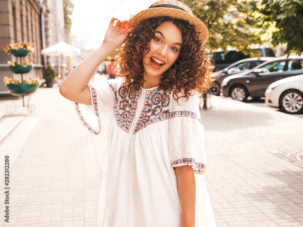 Portrait of beautiful smiling model with afro curls hairstyle dressed in summer hipster white dress.Sexy carefree girl posing in the street background.Trendy funny and positive woman in hat