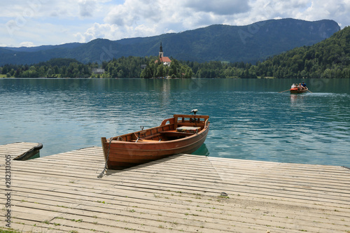 Lake Bled with traditional boat. Beautiful mountain lake in summer with small Church on island with castle on cliff and alps in the background.