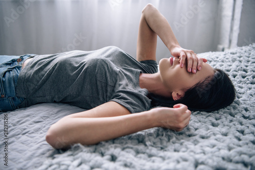 depressed woman lying on bed and covering eyes at home