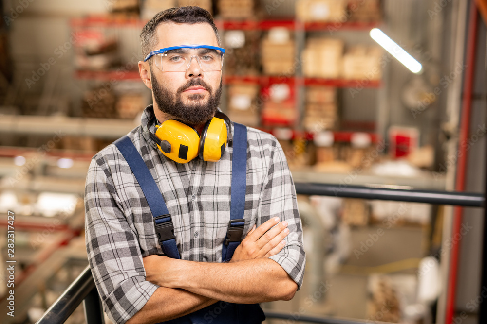 Fototapeta premium Serious warehouse worker in protective eyewear and headphones