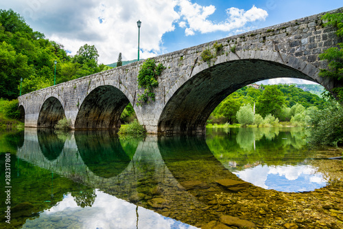 Montenegro, Beautiful ancient stone bridge over river crnojevica near town cetinje in skadar lake national park reflecting in silent glassy water photo