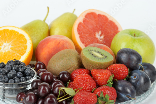 In a plate are orange, grapefruit, cherry, plum, pears, peaches, apple, plum, blueberries, kiwi. Light background. Close-up. Macro shot.
