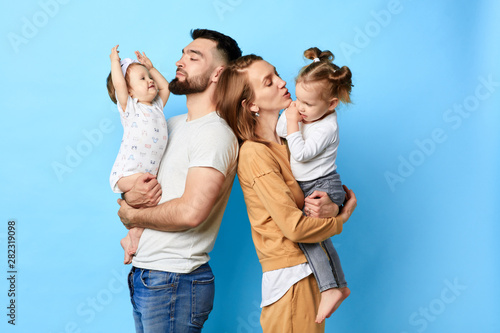two caring parents standing back to back and holding their children in arms. close up photo. isolated blue background. studio shot. photo