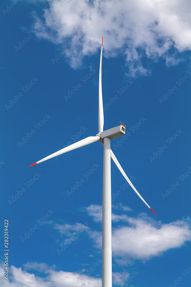 A wind turbine and blue sky with clouds. Large three-bladed horizontal-axis wind turbines produce the overwhelming majority of windpower in the world today.