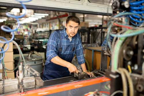 Young factory mechanic or technician working with one of industrial machines