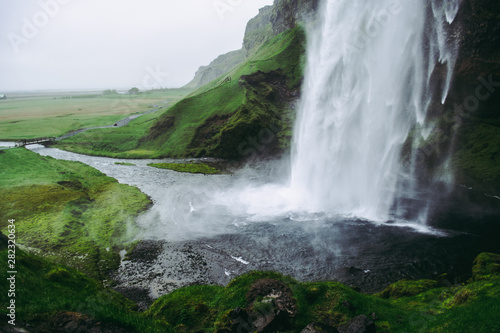Cold pale white water of Seljalandsfoss waterfall in Iceland. Typical windy weather.