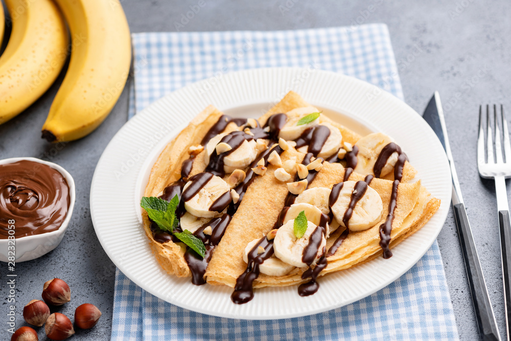 Tasty crepe with banana and chocolate sauce on white plate. French thin pancakes or russian blini for dessert