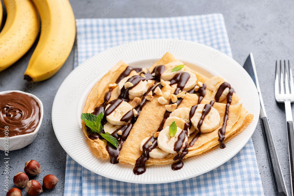 Tasty crepe with banana and chocolate sauce on white plate. French thin pancakes or russian blini for dessert Tasty crepe with banana and chocolate sauce on white plate. French thin pancakes or russian blini for dessert