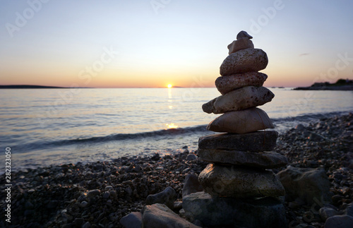 Stacking stones on the empty pebble beach at summer sunset