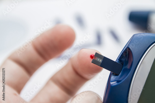 Man takes blood from the finger using the test strip for checking blood sugar level by blood glucose meter. Diabetes concept. Lancet pen and test strips on the background. Closeup, selective focus