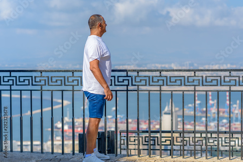 Fototapeta Naklejka Na Ścianę i Meble -  Senior athletic man standing on coastline and enjoying beautiful view at sea. Traveling along coast, freedom and active lifestyle concept.Business smiling beach man in shorts and t-shirt on vacation.