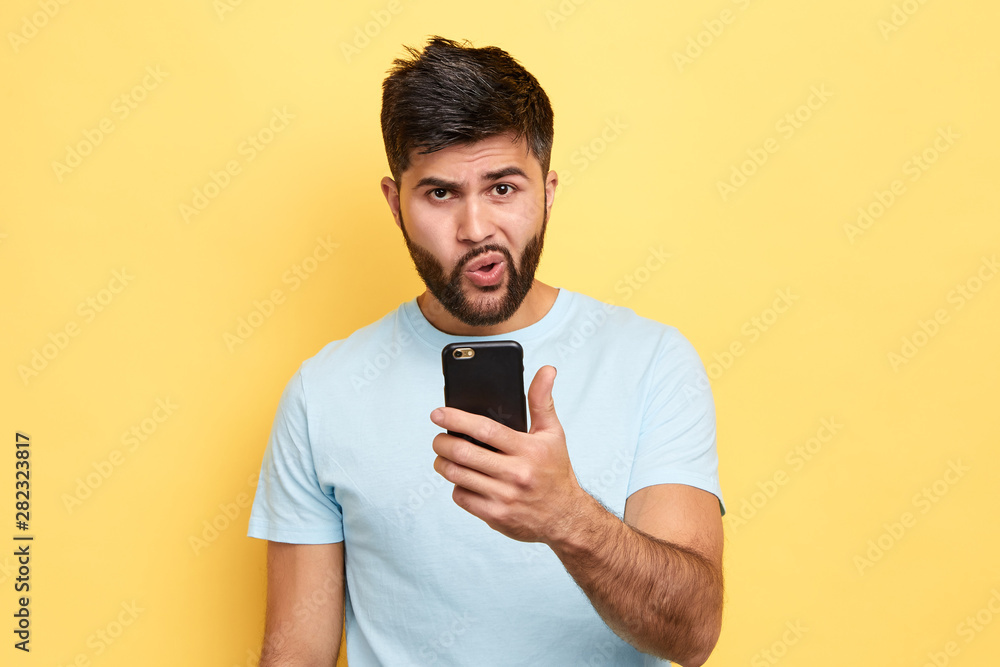 puzzled guy using his mobile phone. close up portrait. young bearded man has problems with gadget, trying to solve it. broken phone puzzled guy using his mobile phone. close up portrait. young bearded man has problems with gadget, trying to solve it. broken phone