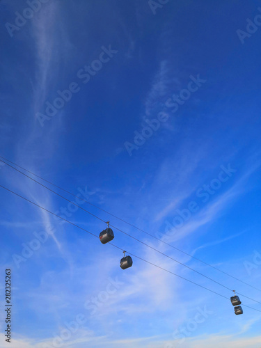Cable car with moving cabins on the background of a beautiful blue sky. View of the funicular from below.