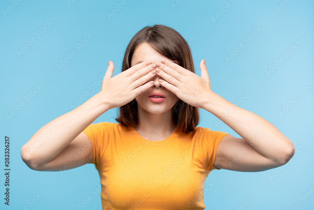 Young brunette female in yellow t-shirt covering her eyes with hands Young brunette female in yellow t-shirt covering her eyes with hands