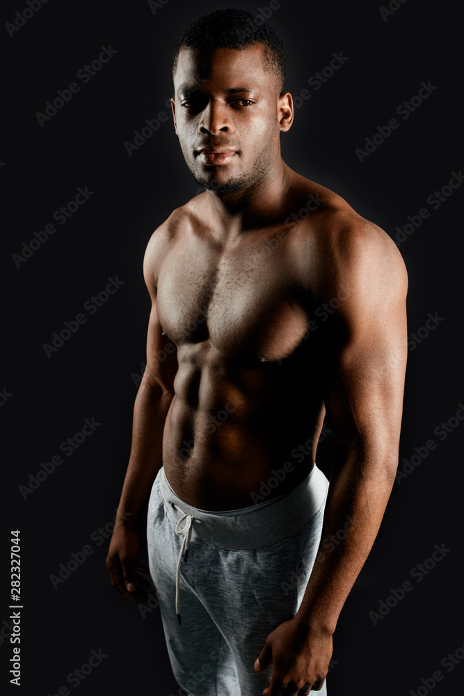 Fototapeta premium pleasant handsome african guy with beautiful body standing over black background.appearance, people concept