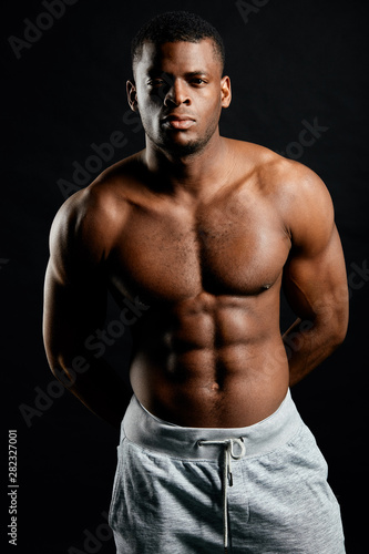 muscular serious bodybuilder with hands on his back looking at the camera. body and health care, beauty.isolated black background. close up portrait. © the faces